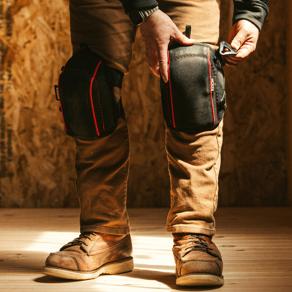 [First name], tile setter, adjusting the thigh strap on the leg, buckle and strap length visible, work pants, head in frame. Callout: "adjustable both sides".