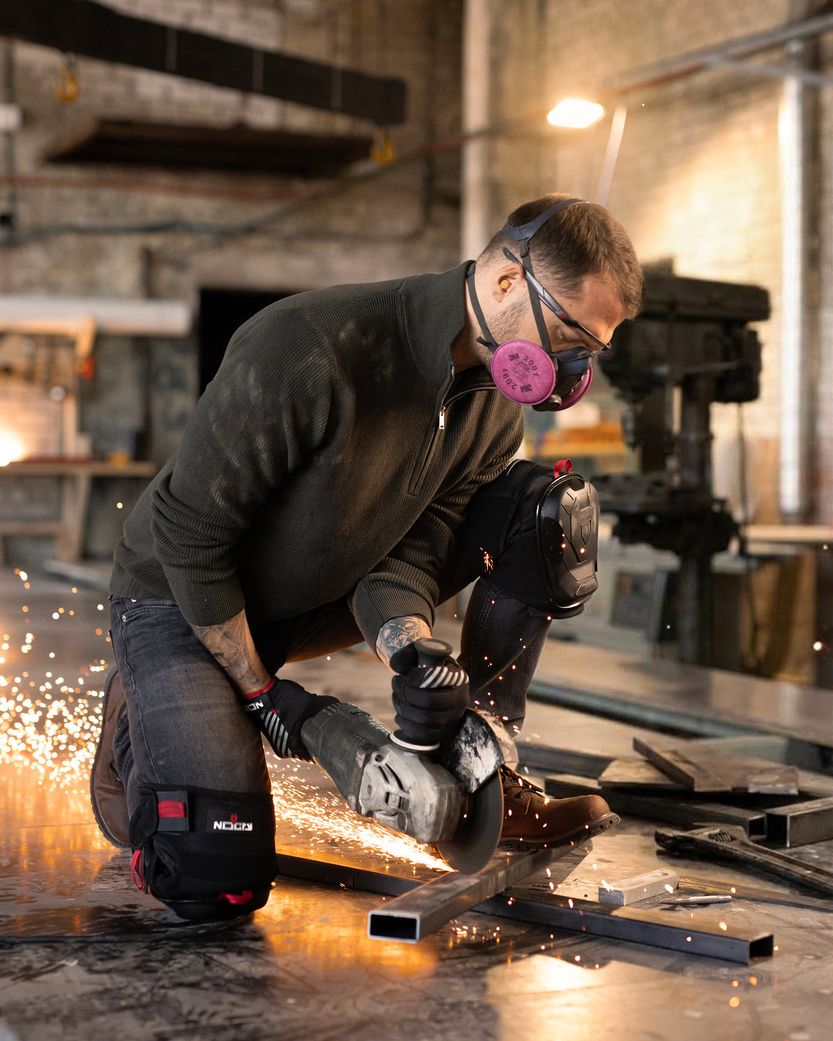 Raino Raasuke on a jobsite, gear on, looking at a prototype pad in his hands, not the camera. Shop light, dust.